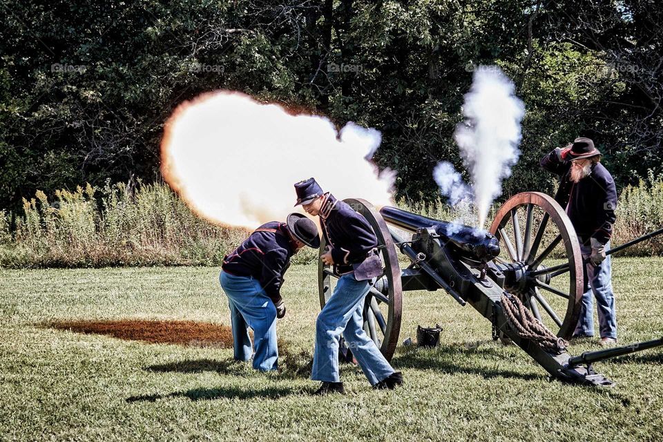 Civil War reenactment firing a cannon in Union uniforms in a field during the summer.