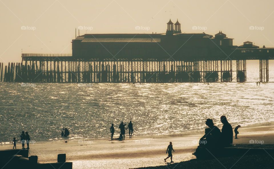 People silhouetted in Hastings beach with the old pier in the distance.