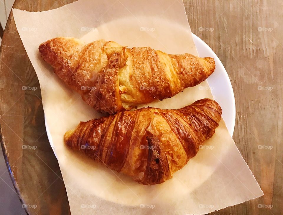 Two croissants on white plate and craft paper on wood table top view 