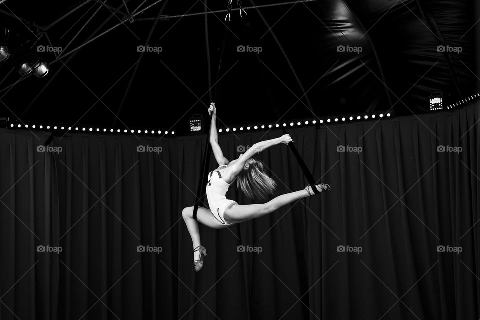 a black and white portrait of a professional circus artist performing an elegant trick on ropes.