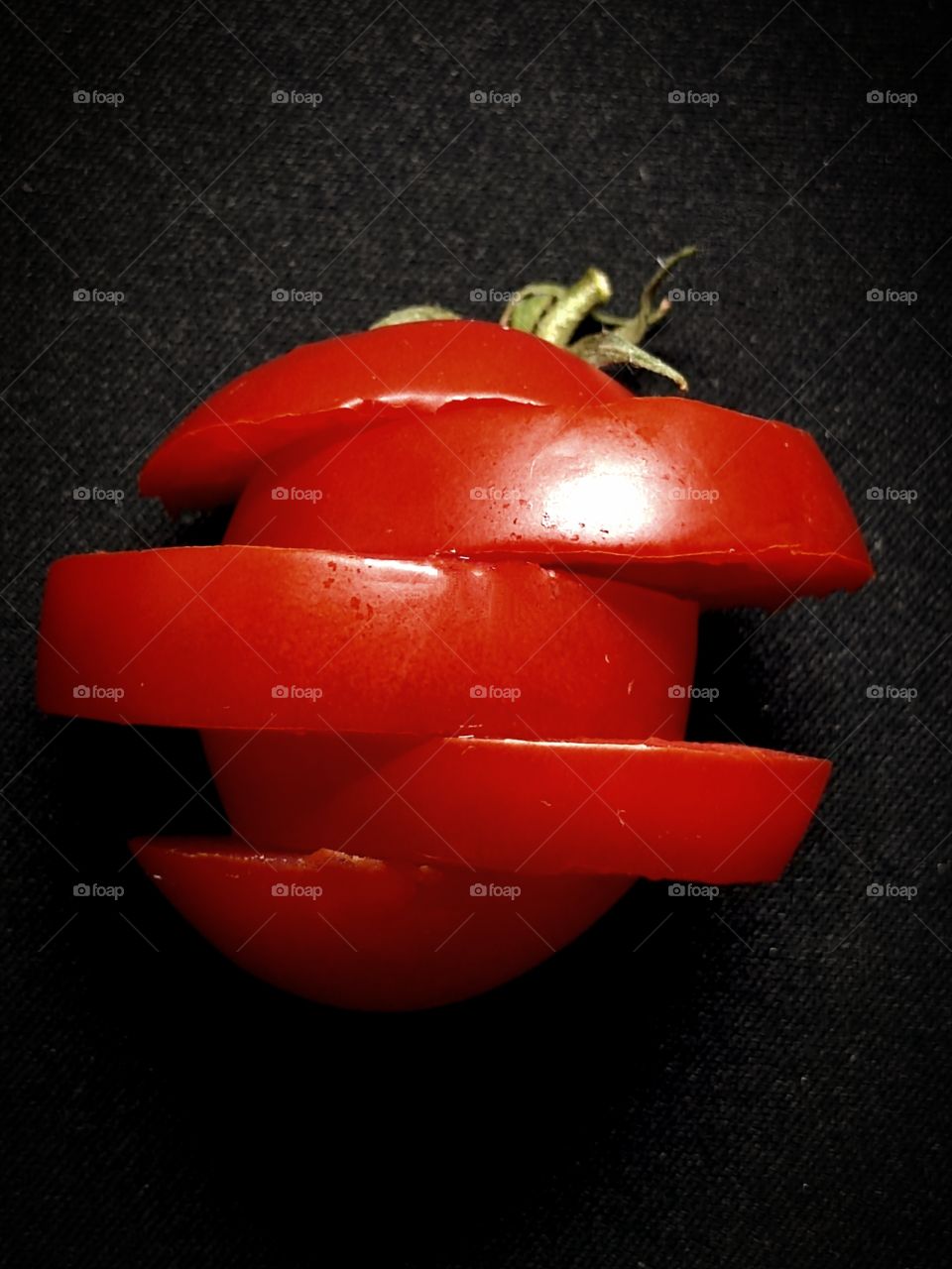 Cherry tomato is cut into wedges.  Irregular tomato shape. Dark background