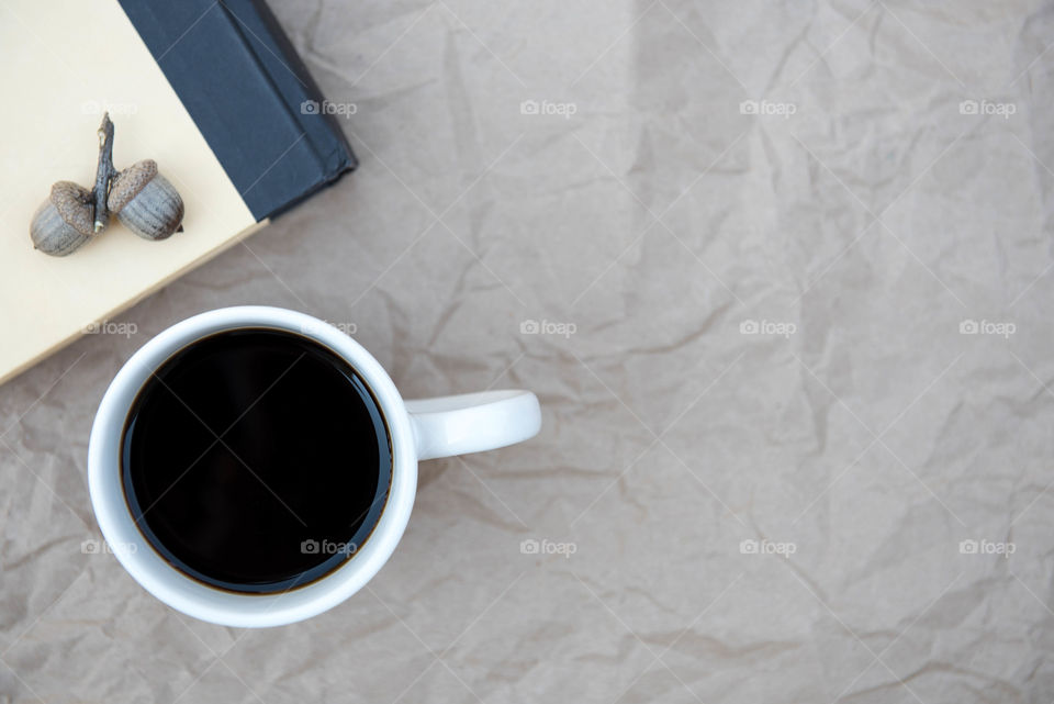 Monochromatic flat lay of a cup of coffee next to a brown book and acorns on a textured brown surface