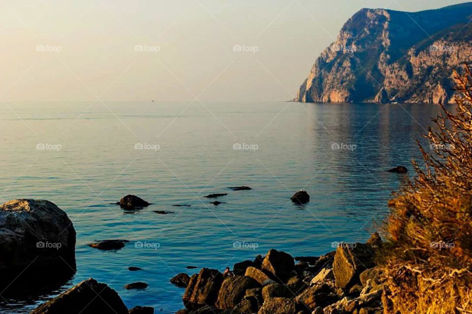 Long distance view of beautiful natural scenery with a backdrop of mountains and calm sea, as well as rocks on the shore