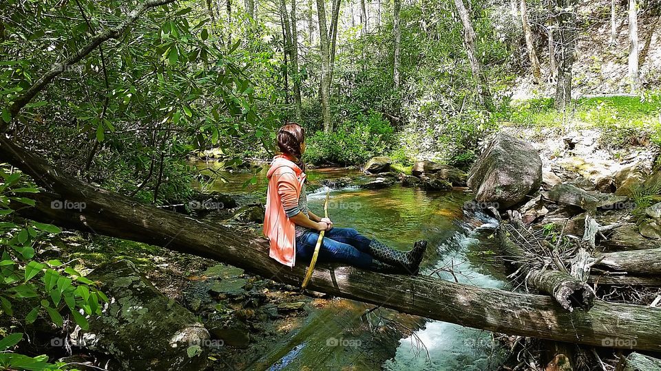woman sitting on a downed tree over a creek