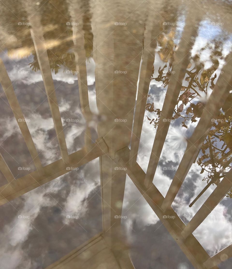 Reflection of fence and sky in the water puddle on ground. 