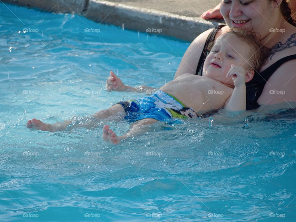 An unhappy toddler boy at the outdoor swimming pool for his first round of swimming lessons on a sunny summer evening. 