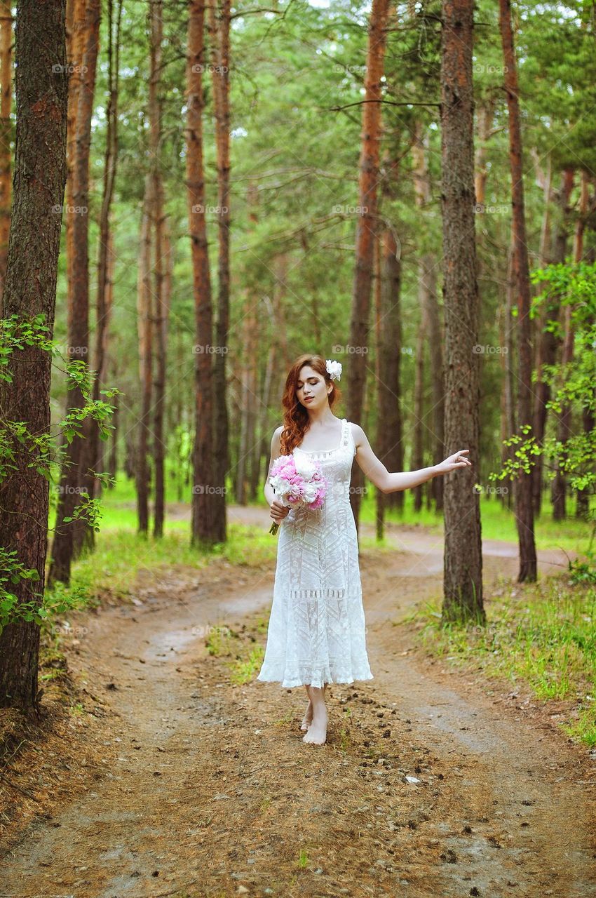 Lifestyle portrait of beautiful redhead bride in white wedding dress with bouquet of pink peonies in summer