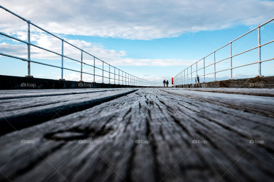 Low angle shot of Victorian British pier with two small figures walking towards the camera
