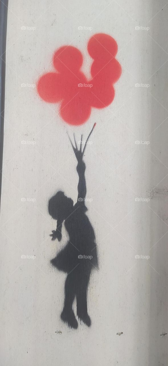 A stencil made on the wall of a Banksy exhibition represents the drawing of a little girl who flies away clinging to several red balloons. this exhibition takes place in Brest, France, in June 2023.