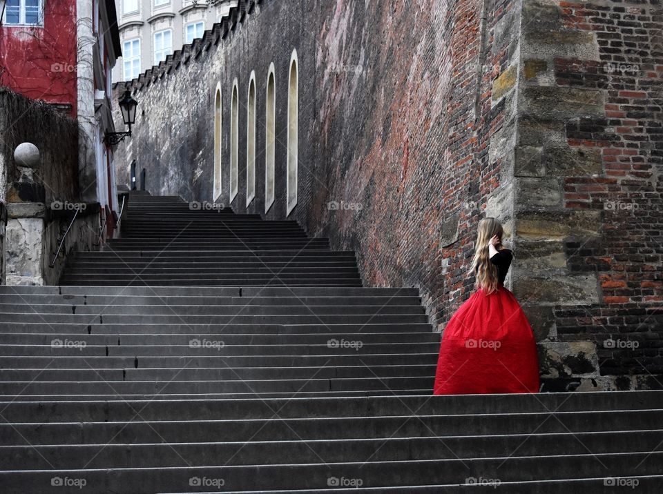 Blonde long hair woman in long red skirt standing on the stairs in old Prague