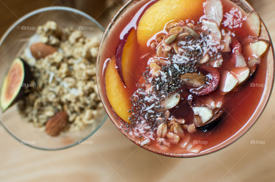 Elevated view of fresh summer fruit smoothie bowls with healthy ingredients garnished with nectarine, ginger, oatmeal, chia seed, black cherry, coconut, almonds and sunflower seeds 