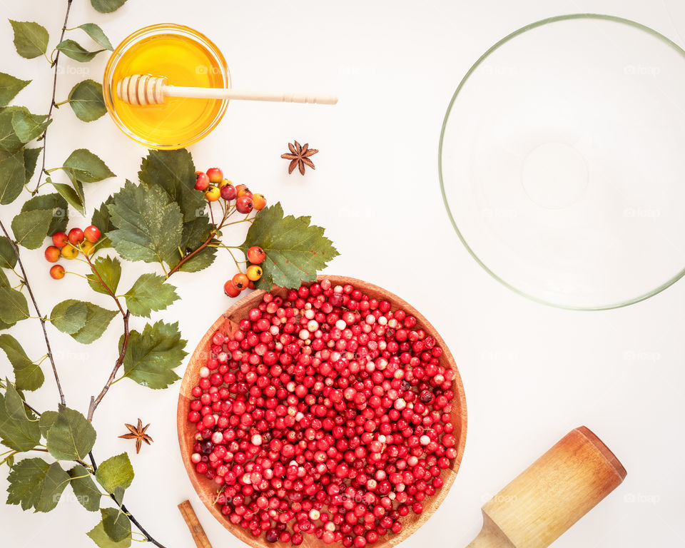 Cooking mors composition with wild cranberries, honey, hawthorn branches and empty glass bowl on a white background. Immune boosting food. Harvesting for the winter, fermenting berries with honey