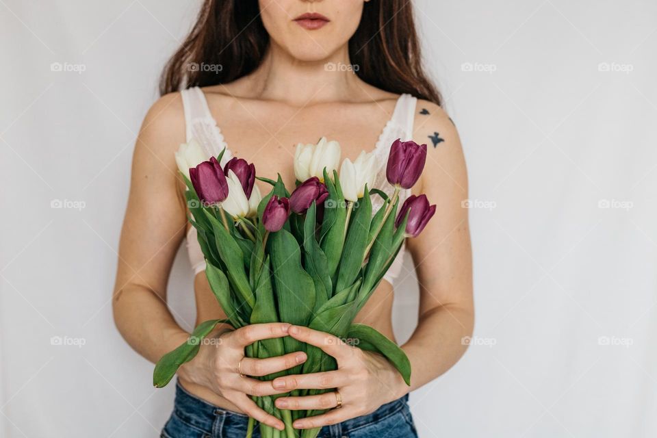 Young woman holding white and purple tulips close to her body, in celebration of women’s day.