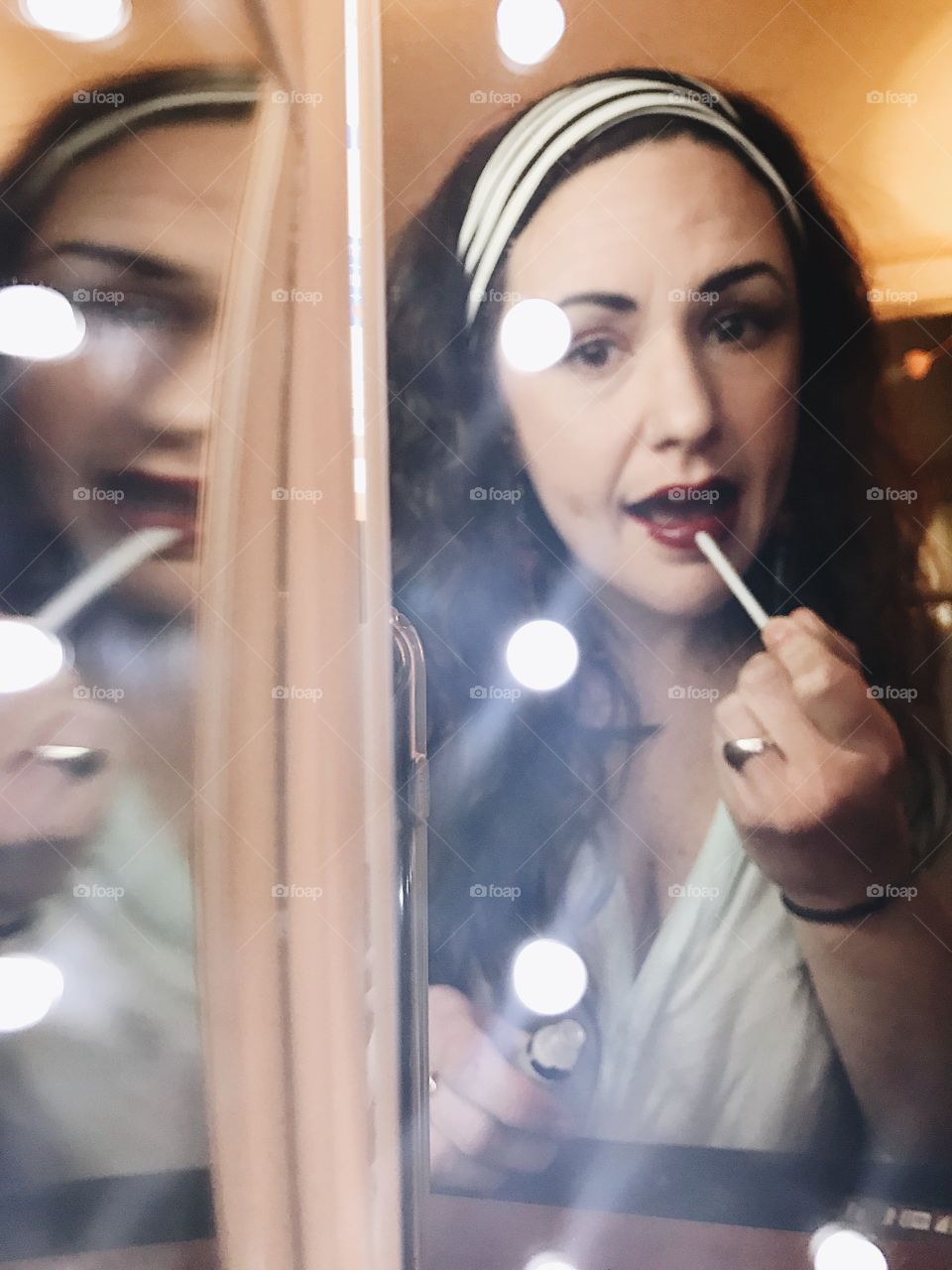 Looking in the lighted mirror and putting on my lipstick with my long, curly hair down and tied back with a headband. 