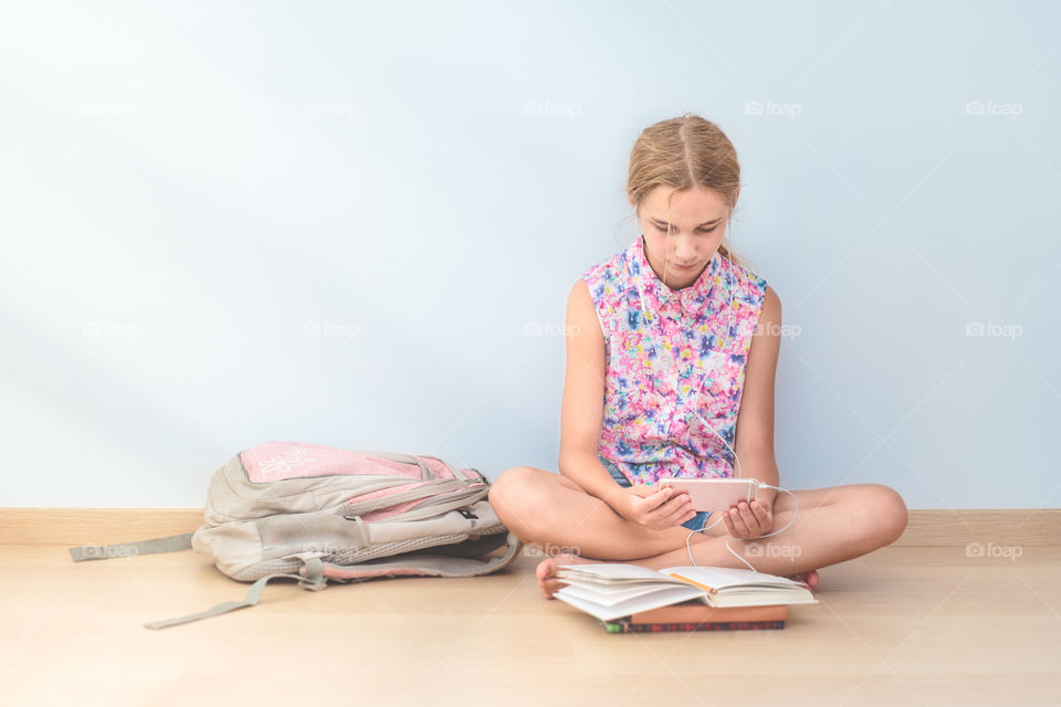 Teenage girl listening music with books on hardwood floor