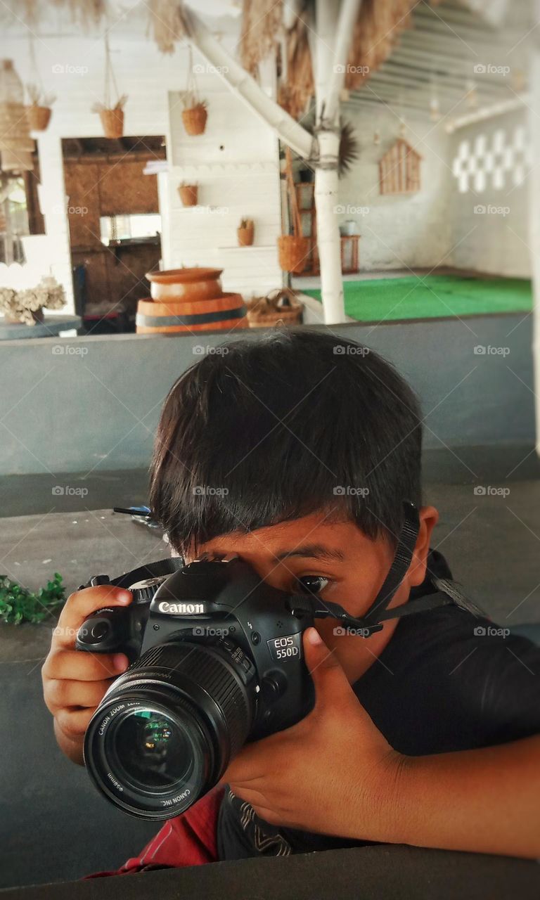 model anak laki laki melakukan photo dengan kamera Canon 550D 
warna hitam model kamera Canon 550D