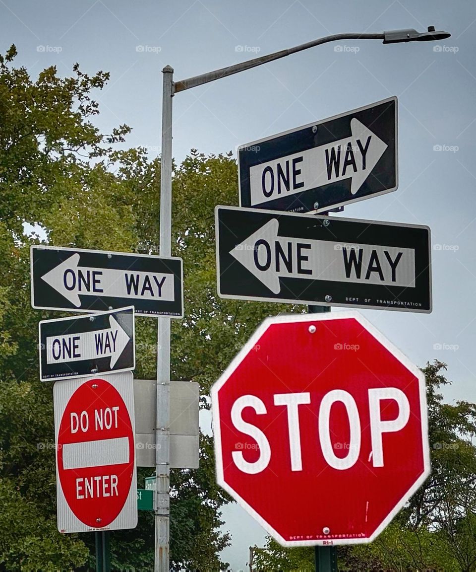 Conglomeration of traffic signs with One Way signs pointing in different directions 