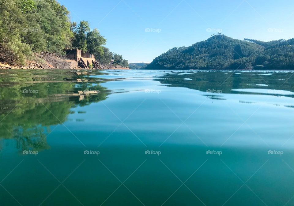 View from on the river of blue sky reflected in the water and tree covered hills in the distance 