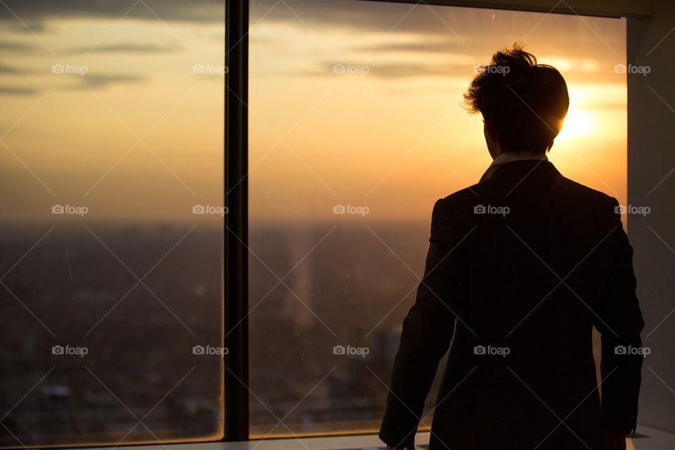 A young man looking outside a massive window into the bright sun