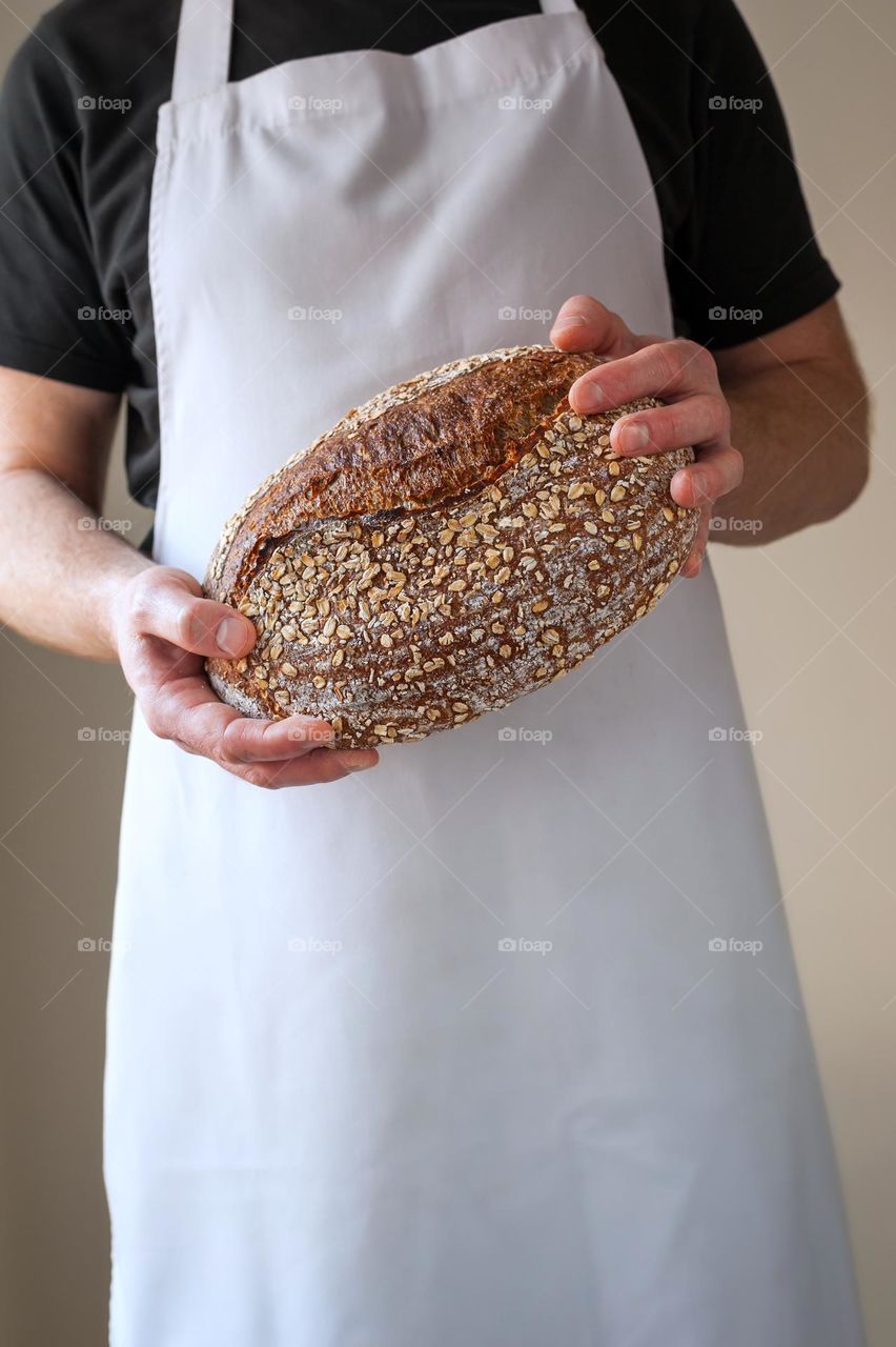 Close-up at bakers hands holding a loaf of sourdough bread in front of him.