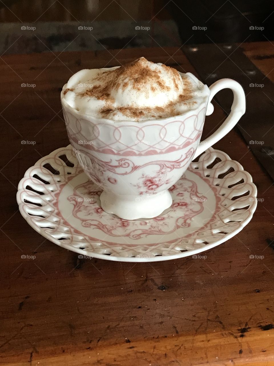 An elegant cup of coffee served in a teacup, with heaping foam and cinnamon on a wooden table.