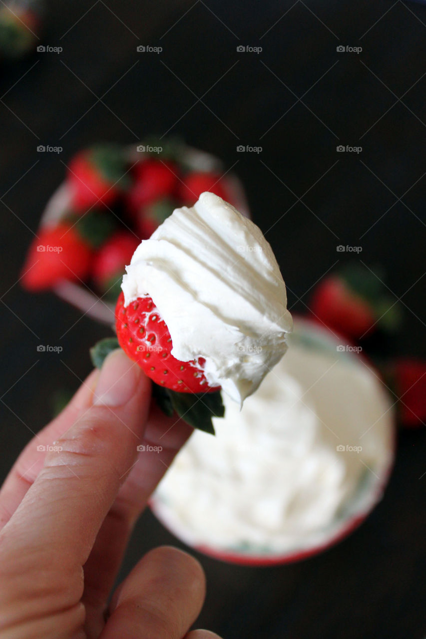 Human hand holding strawberry with cream