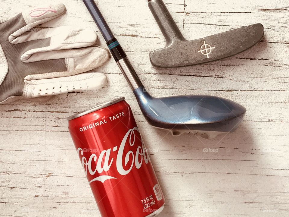 A can of Coca Cola and golf equipment on a rustic white background 