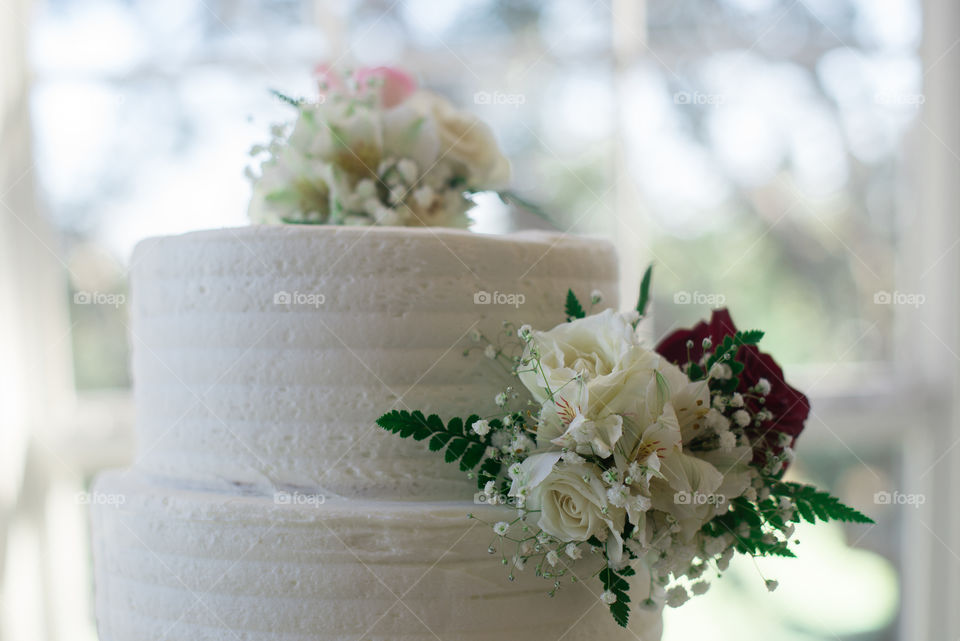 White three tier cake with pink and red roses near window