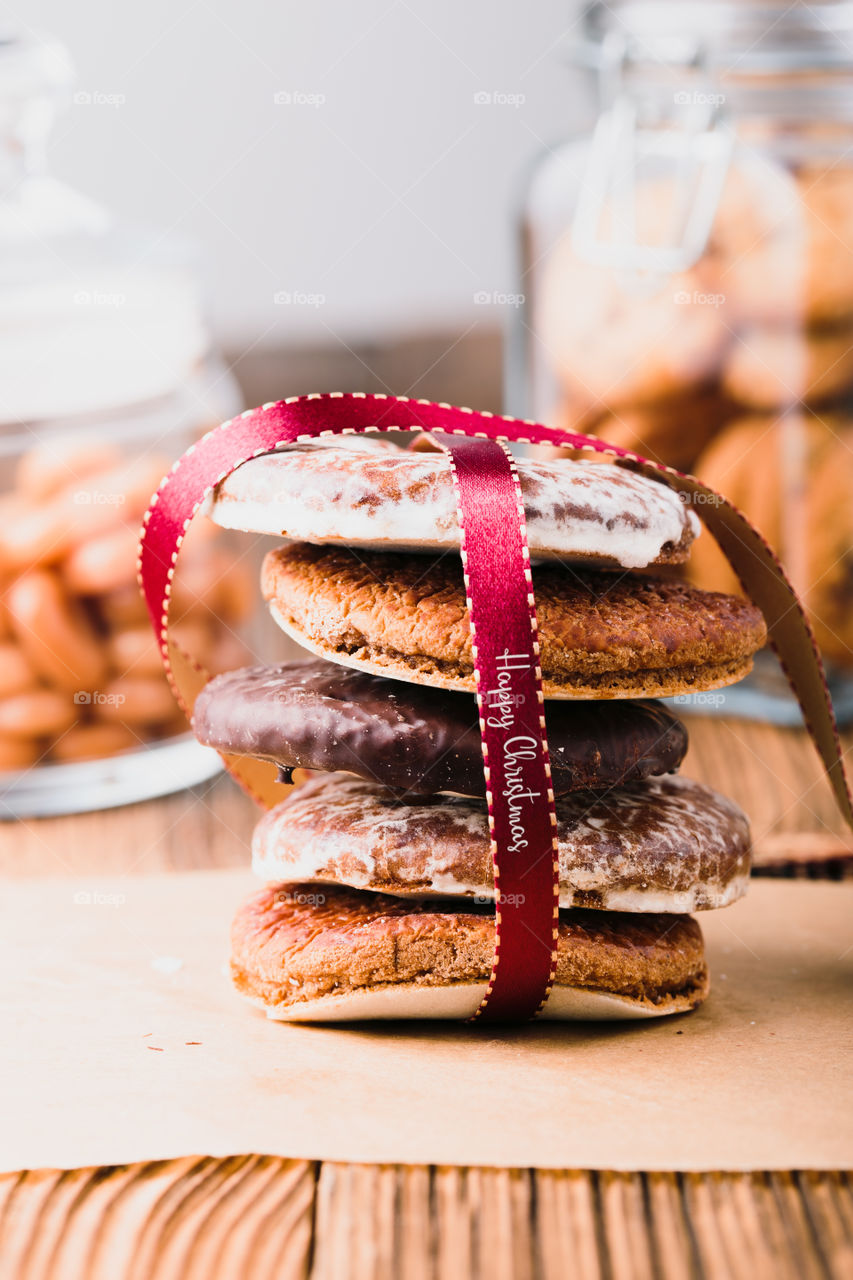 A few gingerbread cookies wrapped in red ribbon Happy Christmas on wooden table. Jars with sweets in the background. Portrait orientation