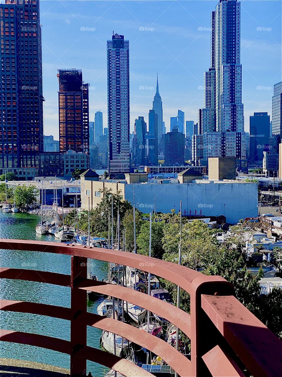 This is a spectacular view from the top of the „Pulaski Bridge“ at „Newtown Creek“ on the near side of the center outpost. Behind the LIC skyscrapers we see „Manhattan“ including the „Empire State Building“. 2023. Hypnotic Productions