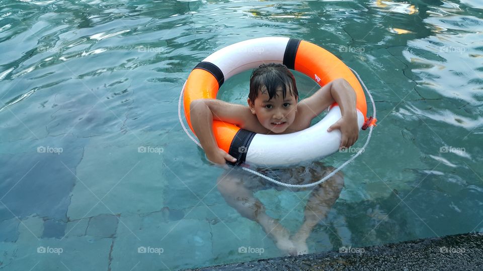 kid safety at pool. young boy swimming with life ring