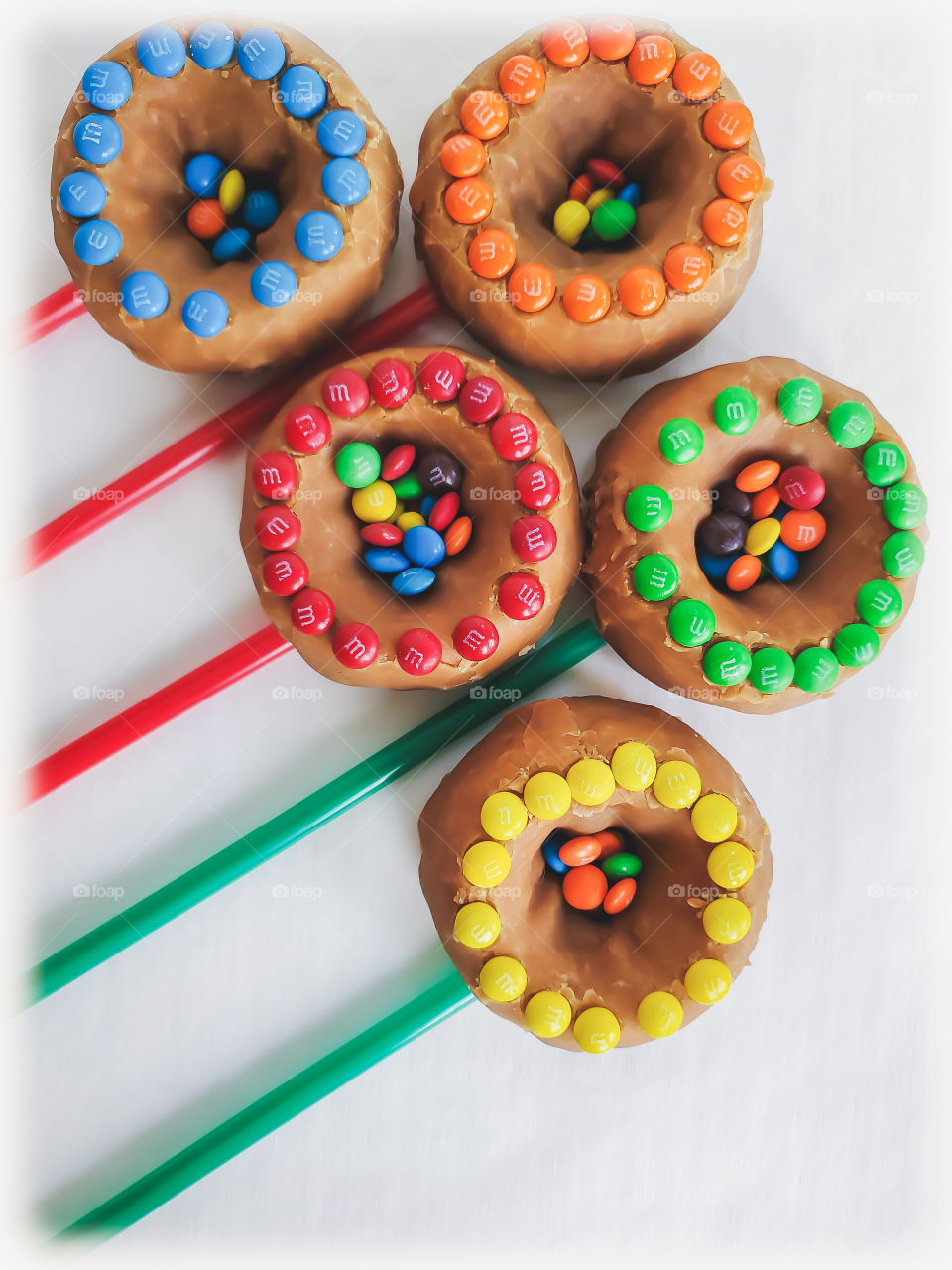 M&M minis decorated donuts filled with peanut M&Ms and mini M&Ms in the center, layed out in a creative bursting/shooting star or flower bouquet design on a white background.