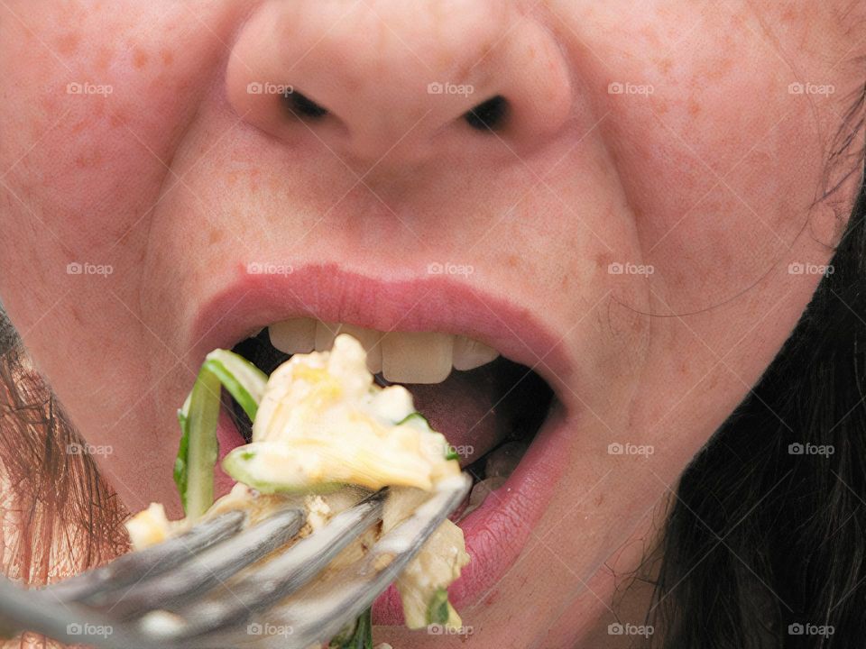 Glimmers close-up of eating a delicious salad with Colby Jack shredded cheese, spring mix lettuce and spinach with parmesan and Italian dressing and mayonnaise on a fork with bowl aside. Mouth opened smiling to eat with hair and grey blue background.