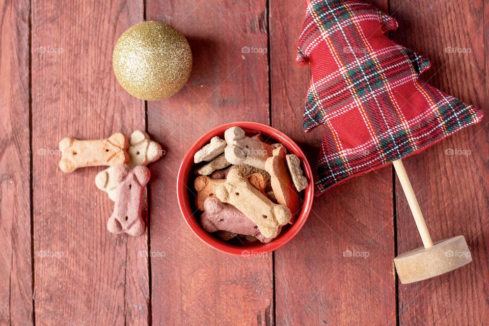 Flatlay of a Red bowl of dog treats for the holidays with a small tree on a wooden backboard 
