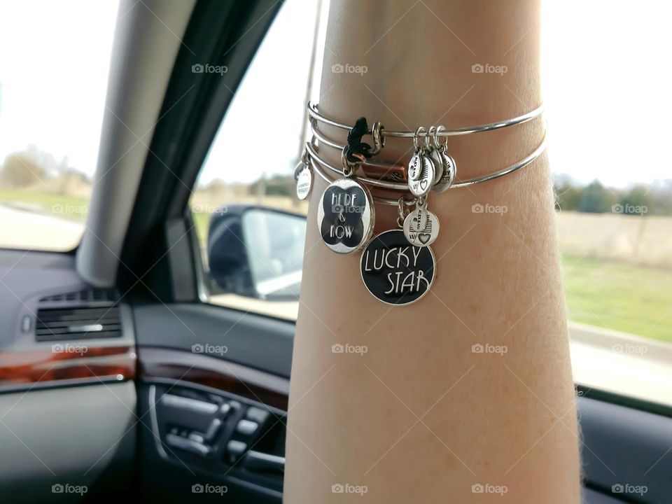 Alex & Ani Silver Bangle Bracelets in a Woman's arm in a car riding down the road