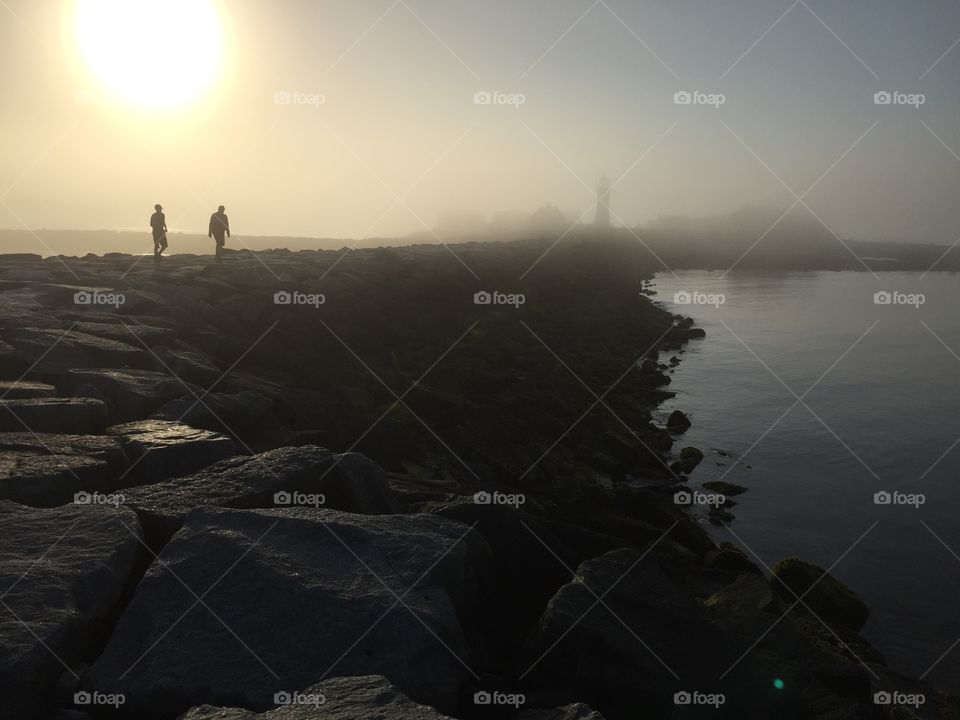 Lighthouse enveloped in fog, silhouettes on jetty 