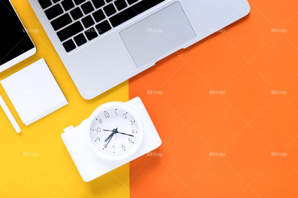 Clock and office device flat lay on bright orange yellow background