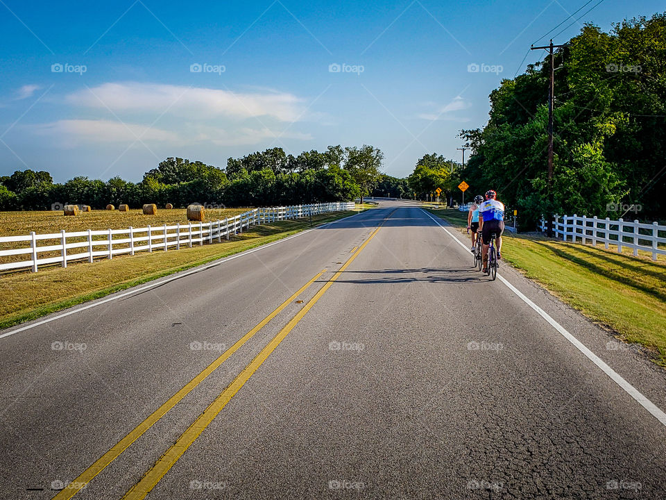 A pair of cyclists riding along a rural highway beside hay fields and farmland
