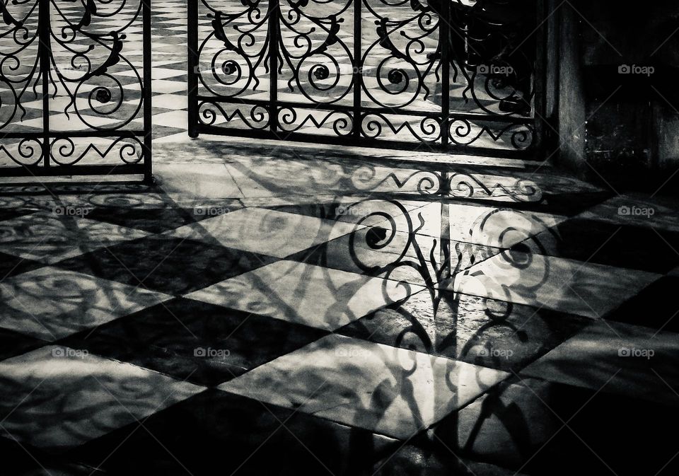 Silhouette of an ornate cast iron gate on a checkered tile floor - inside Notre Dame, Paris