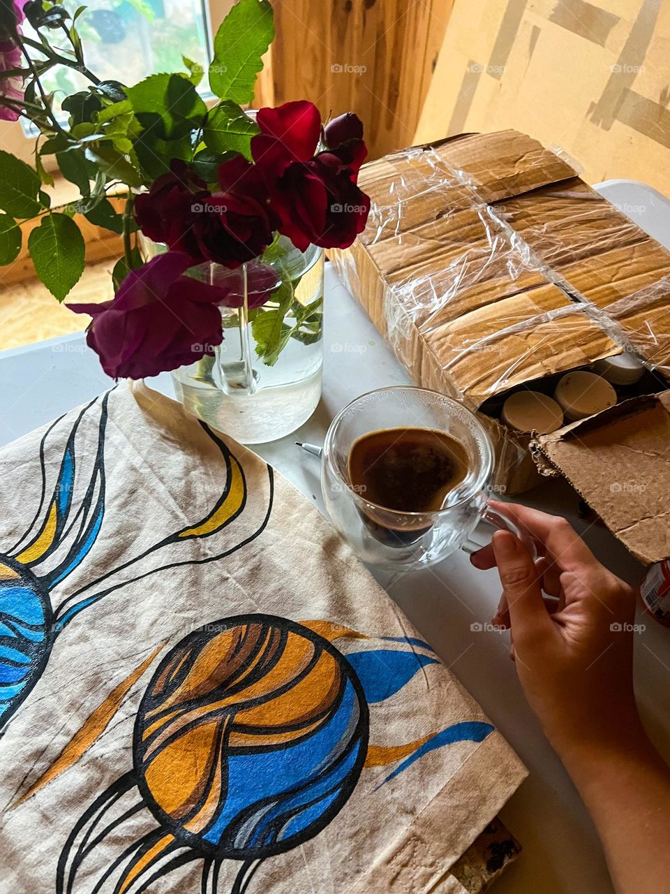 inspiring and tender red roses bouquet in a glass big jar near the artwork process and cup of hot coffe