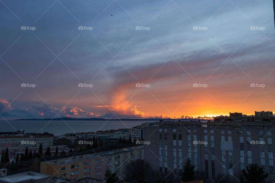 Sun light and clouds at sunset makes magic over sea and a city