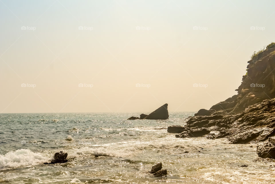 Beautiful sea shore view at sunrise or sunset time. Wild Empty Tropical beach, yellow sand, mountain view, see wave crushing on the rock, sunlight reflection, landscape photo. Travel vacation concept.