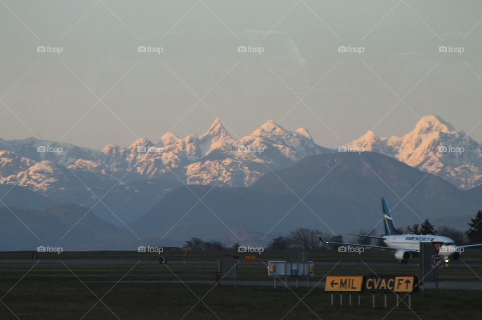 West Jet aircraft landing at West Coast airport with view of the sunset lit Rockies in the background. 