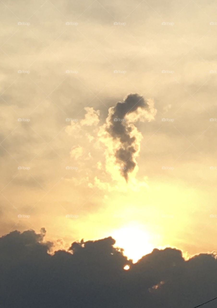 Odd-shaped dark cloud looms above bright sun nestling into more clouds on a steamy July evening