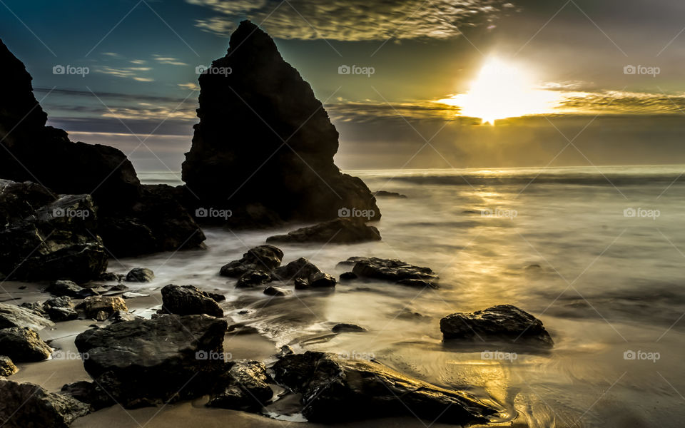 Rocky cliff in sea during sunset