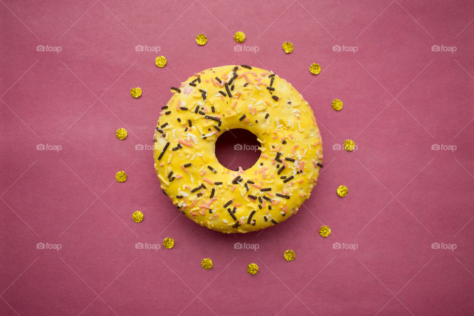 Cute donut background. Yellow donut surrounded by gold confetti on pink background.