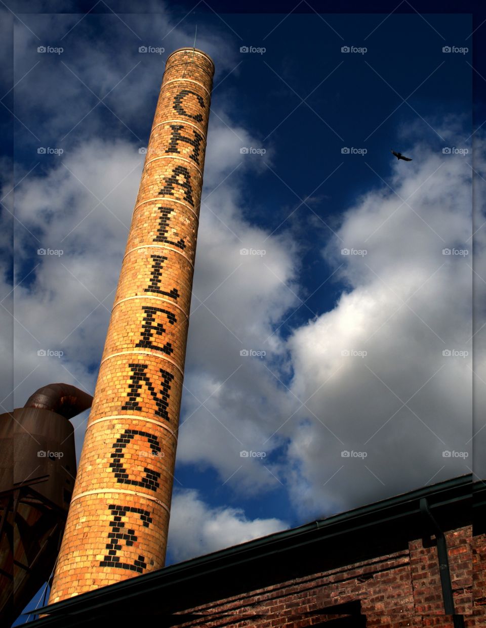 Challenges. A dramatic silhouette of a smokestack against puffy clouds from the old Challenge Windmill factory