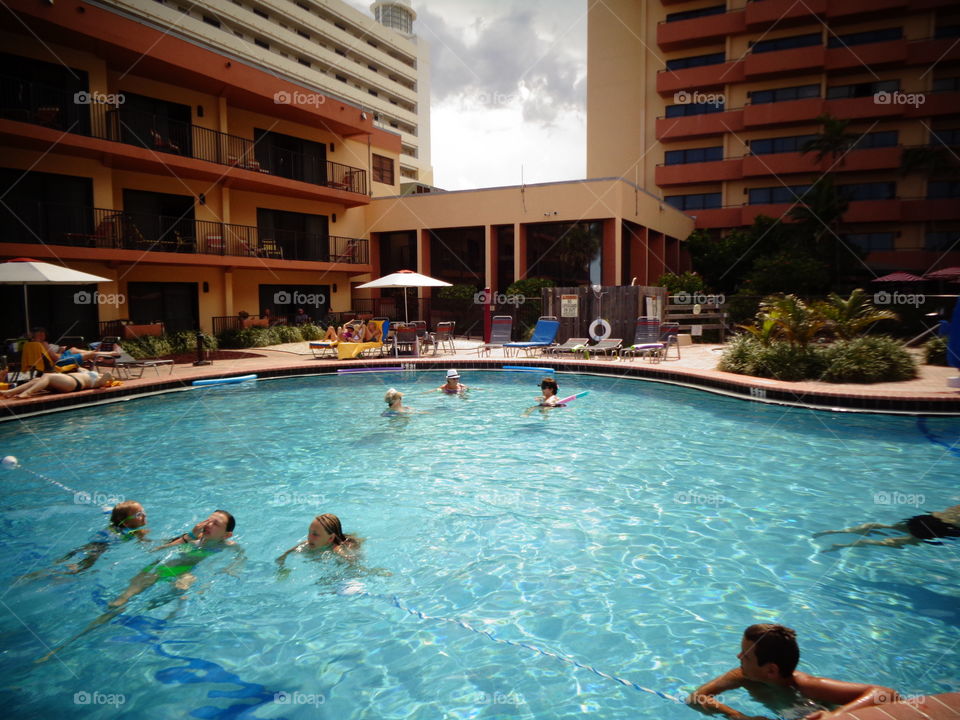 Swimming pool, storm cloud view between two hotel highrise. People enjoying pool water & deck umbrellas.