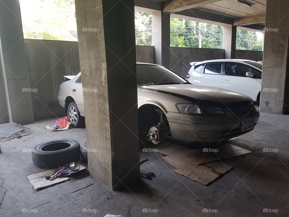 Broken car with missing wheel under repair in a dusty garage