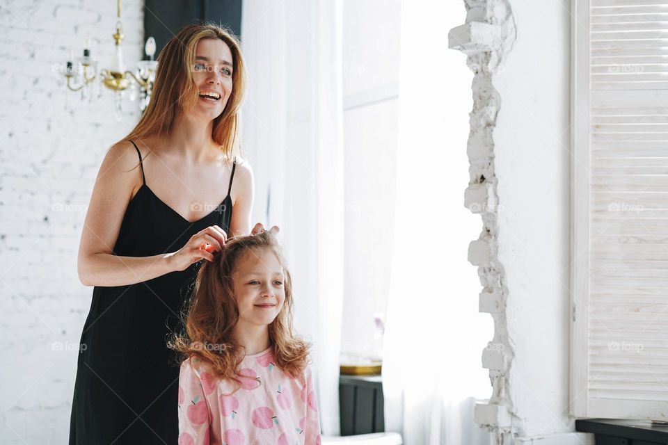 Young mother woman with long hair in black dress and little tween girl daughter in pajamas having fun in the morning at home, family spending time together in bathroom